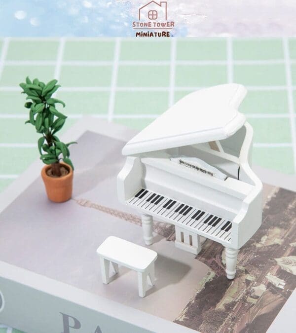 Miniature white grand piano and bench on book with potted plant nearby.