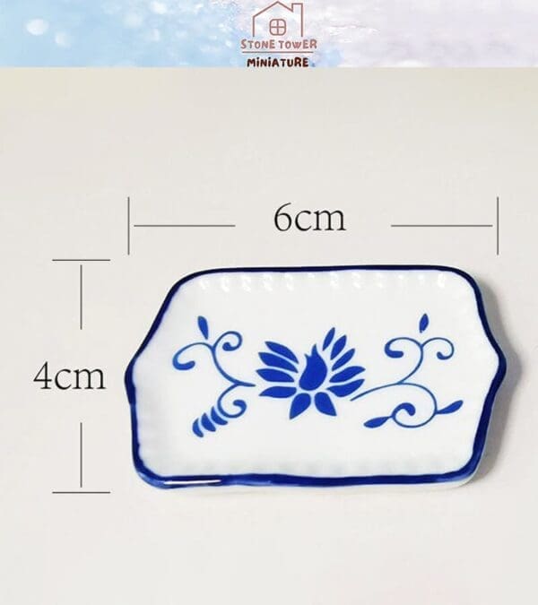 White and blue miniature ceramic plate with floral design; dimensions 6cm by 4cm.