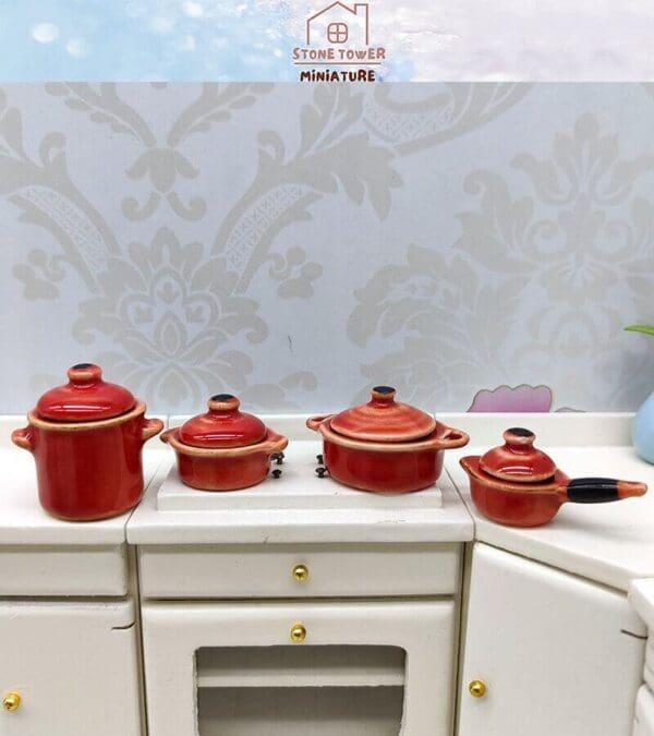 Miniature red cookware set on a small white kitchen counter with floral wallpaper background.