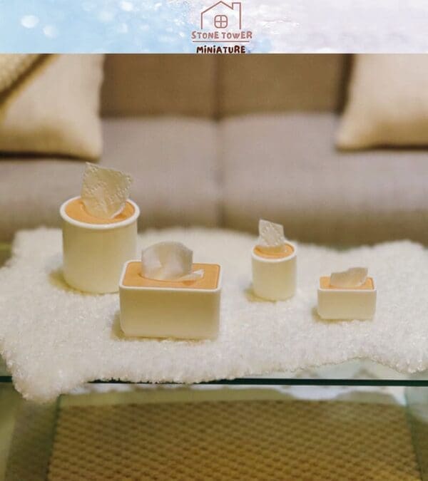 Miniature tissue boxes on a soft, textured surface in front of a blurred sofa, showcasing delicate craftsmanship.