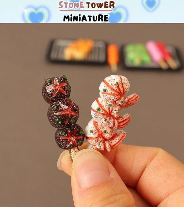 Close-up of a hand holding two miniature candy skewers, one dark and one white, with festive decorations.