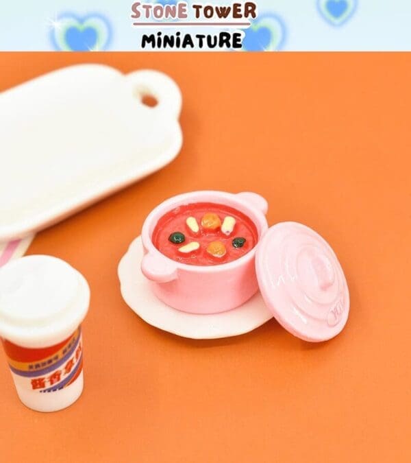 Miniature pink pot with vegetable stew on orange background, next to a small white tray and cup.