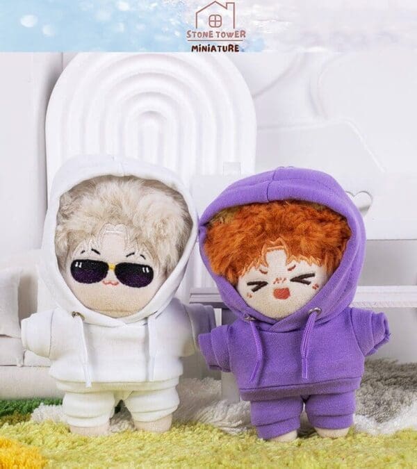 Two plush dolls in hoodies, one white with sunglasses and one purple, stand on a patterned rug.