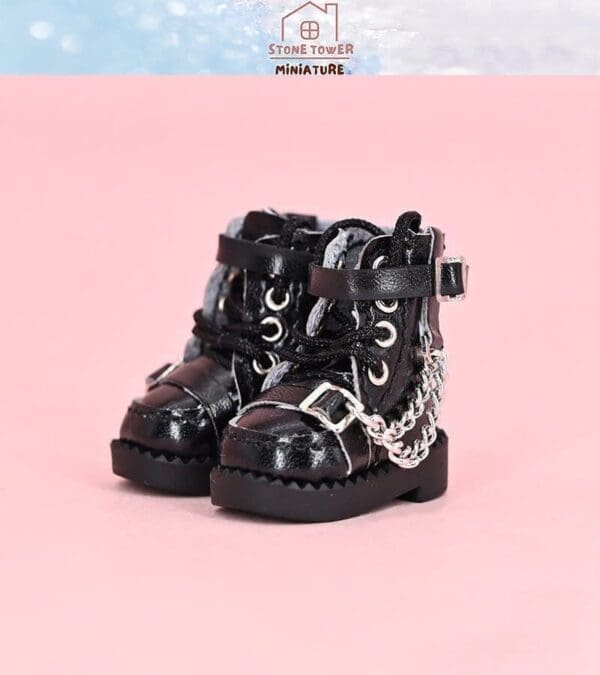 Miniature black boots with silver chains on a pink background.