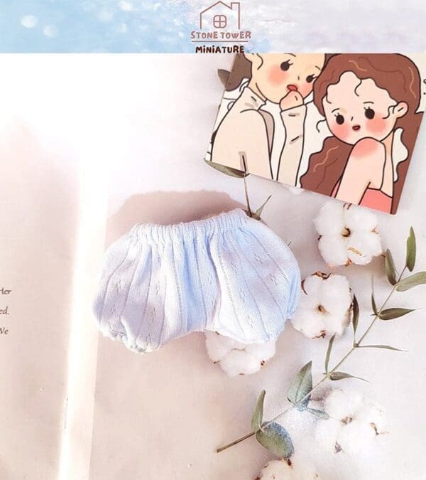 Light blue baby shorts with cotton flowers and a cartoon card on a soft, white surface.