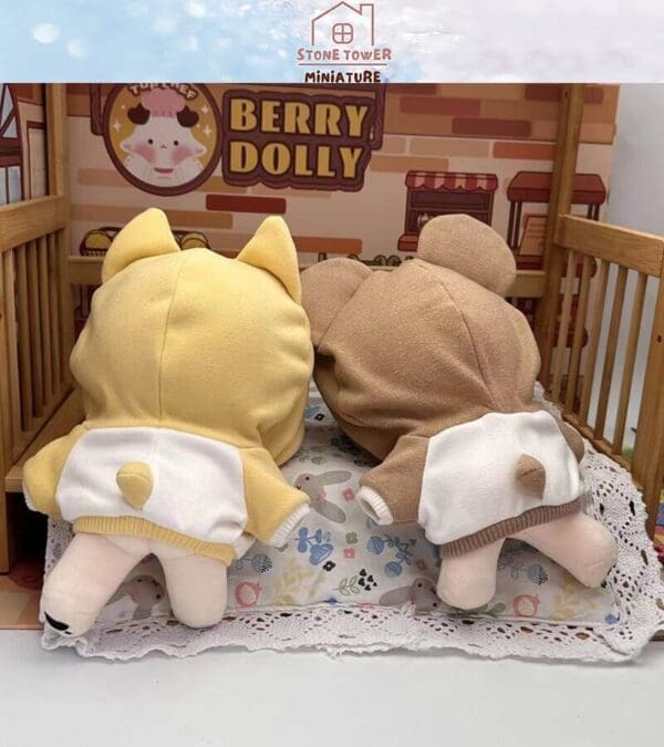 Two plush toys in animal hoodies lying on a decorative bed, with a "Berry Dolly" sign in the background.