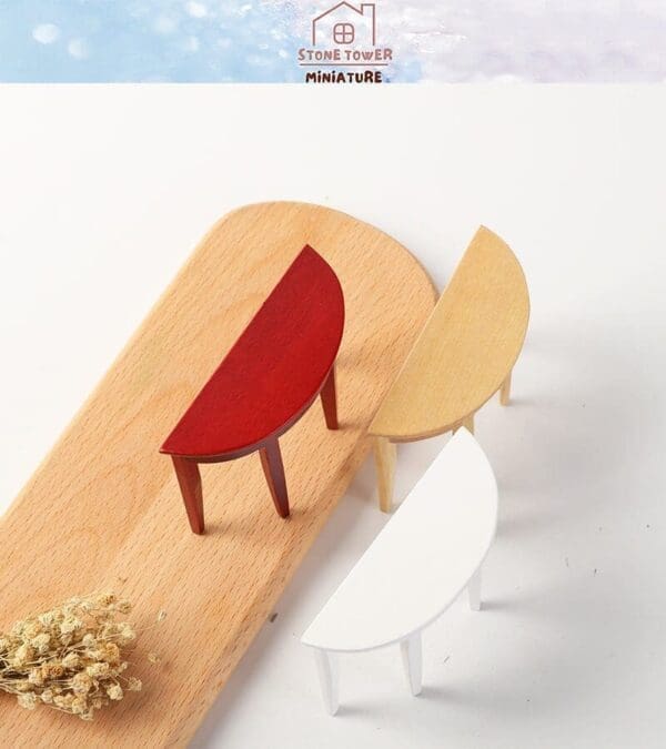 Miniature half-moon tables in red, beige, and white on a wooden board with dried flowers.