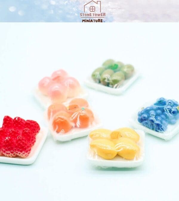 Miniature plastic fruit trays with assorted colorful fruits in clear packaging on a light background.