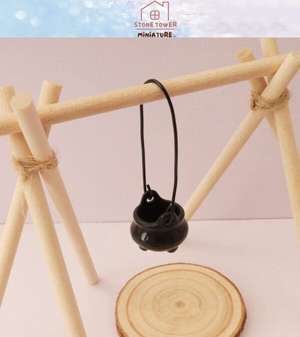 Miniature black pot hanging on a wooden tripod stand over a circular wooden base.