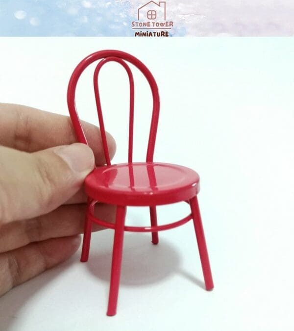 Hand holding a small red miniature chair with a curved backrest.