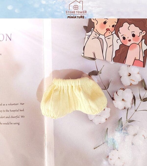 Yellow doll skirt on open book with cotton flowers and a cartoon card nearby.