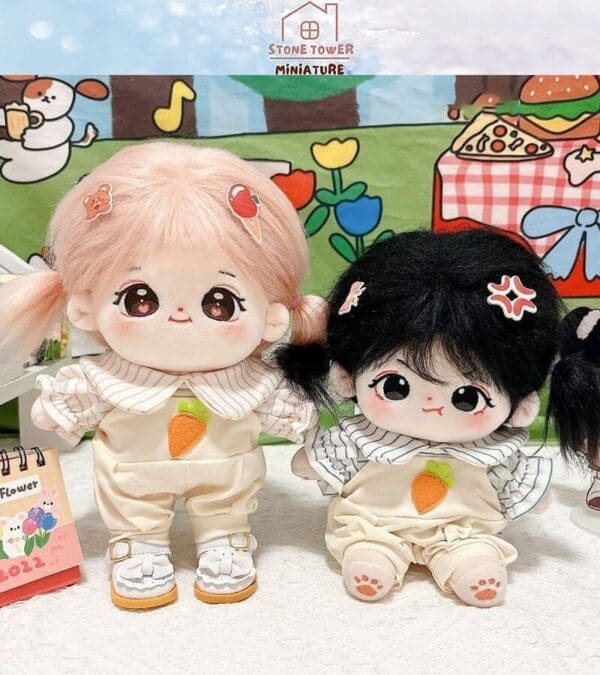 Two cute plush dolls with pigtails and carrot-themed outfits sit on a white surface, against a colorful backdrop.