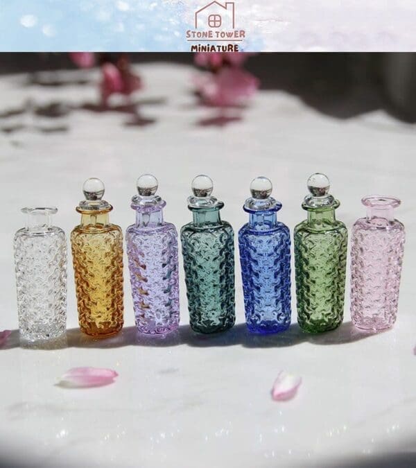 Six colorful glass bottles with textured patterns and round stoppers, arranged on a marble surface with pink petals.