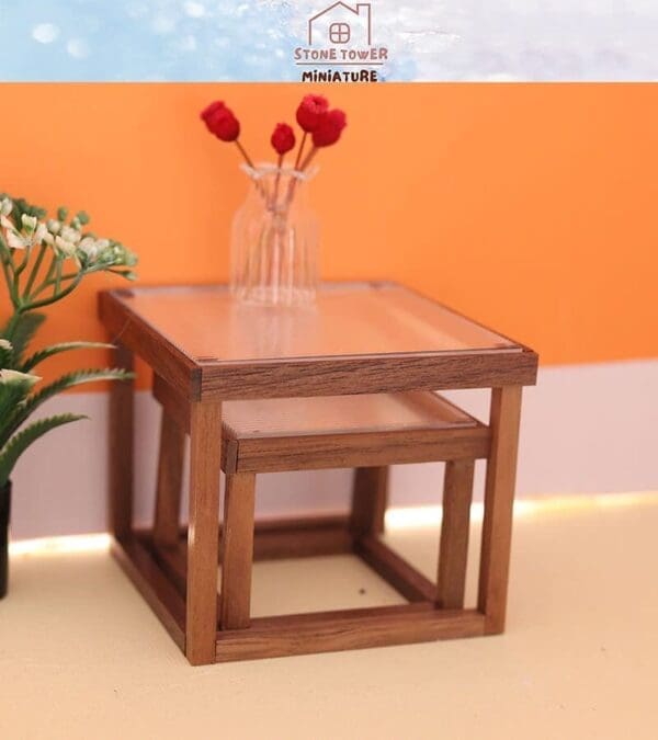 Miniature wooden table with a clear top, small vase with red flowers, and potted plant on an orange background.