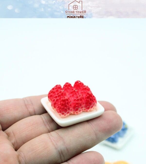 Hand holding a miniature plate of realistic red strawberries against a light background.