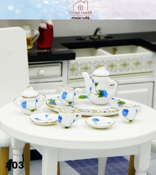 Miniature tea set with blue floral design on a round table, set in a dollhouse kitchen environment.